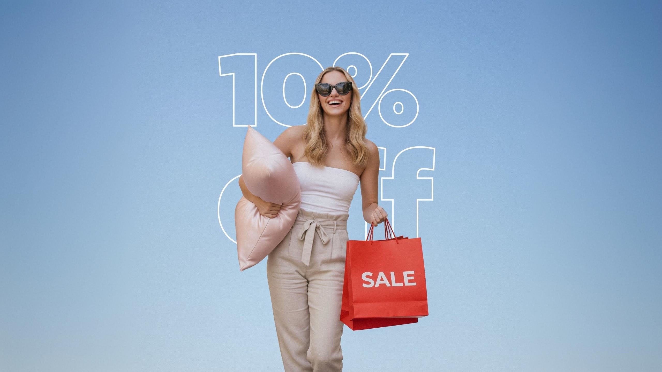 Jeune femme souriante avec lunettes de soleil, sac shopping rouge SALE et coussin rose, fond bleu 10% off